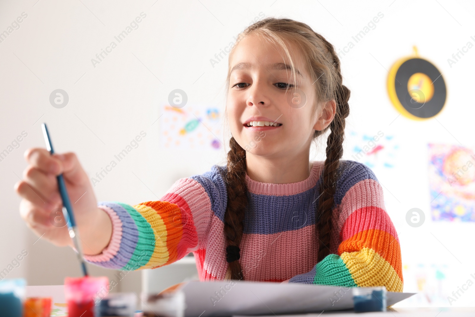 Photo of Little girl painting picture at table indoors