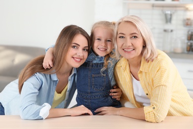 Photo of Portrait of young woman, her mature mother and daughter at table indoors