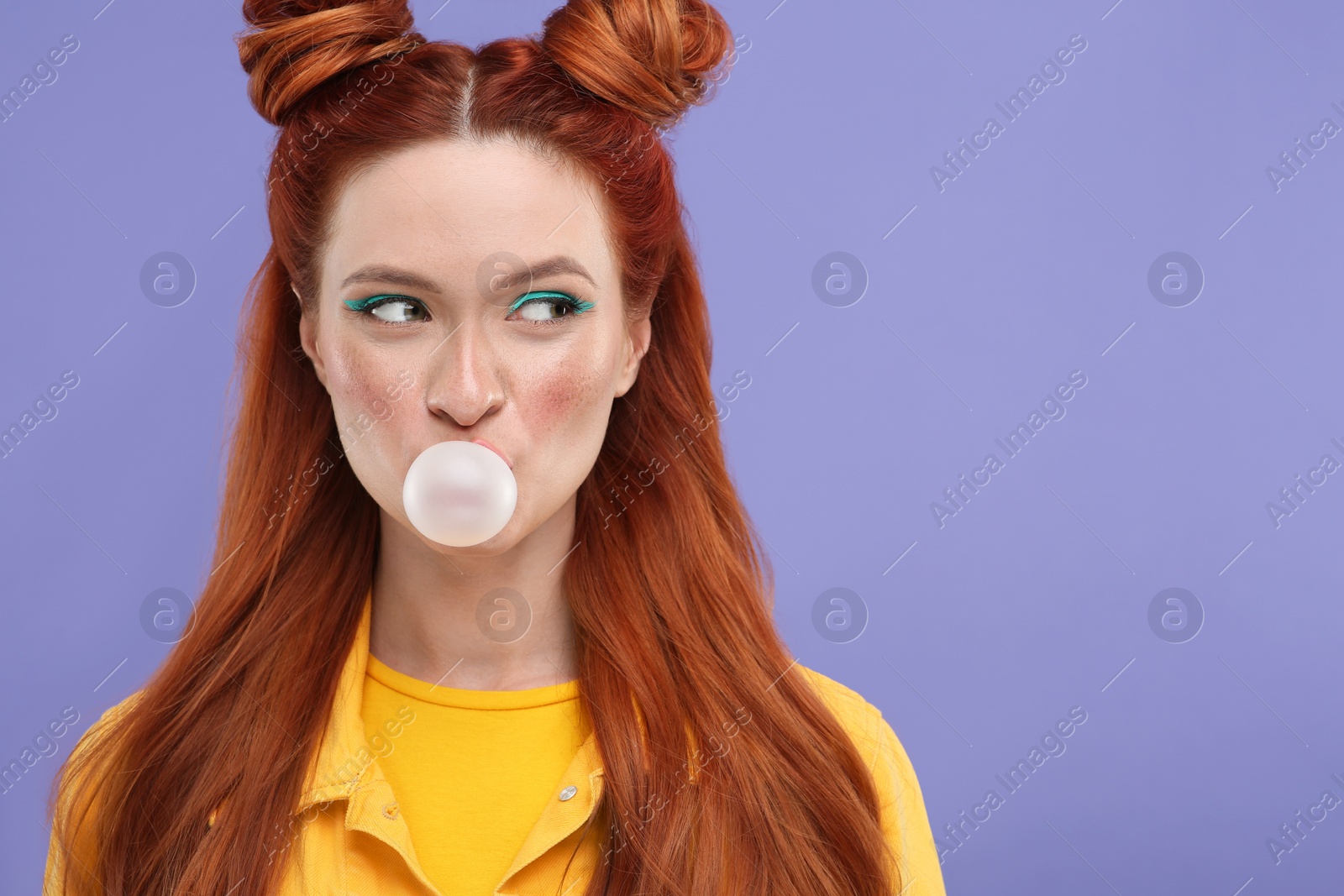 Photo of Portrait of beautiful woman with bright makeup blowing bubble gum on violet background. Space for text