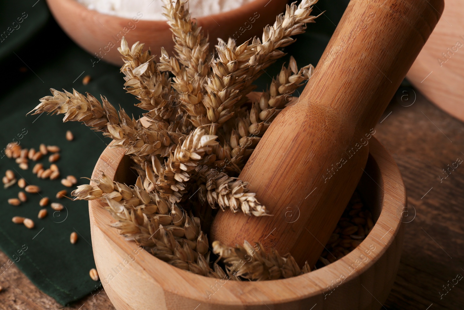 Photo of Mortar with wheat spikes on wooden table, closeup