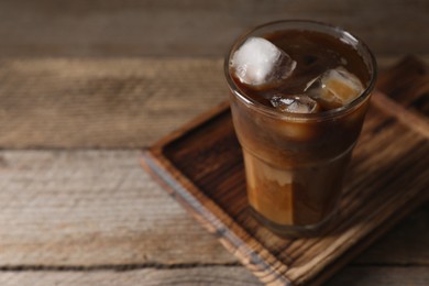 Photo of Glass of delicious iced coffee with milk on wooden table, closeup. Space for text