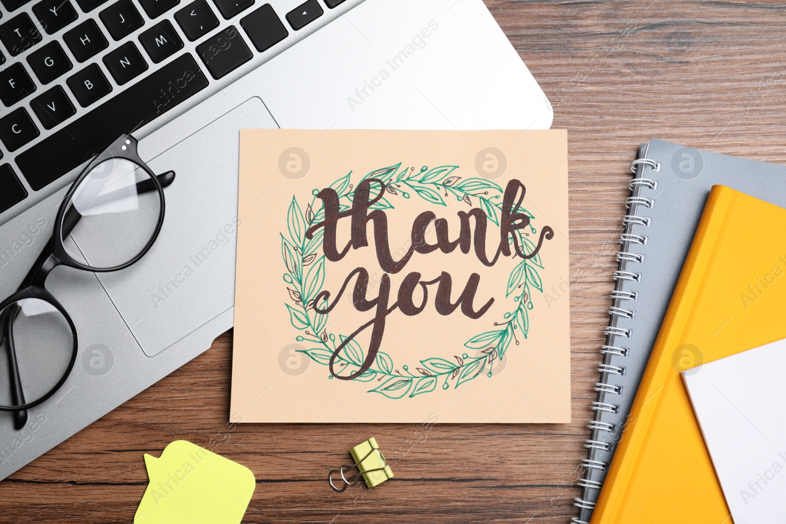 Photo of Card with phrase Thank You, laptop, glasses and notebooks on wooden table, flat lay