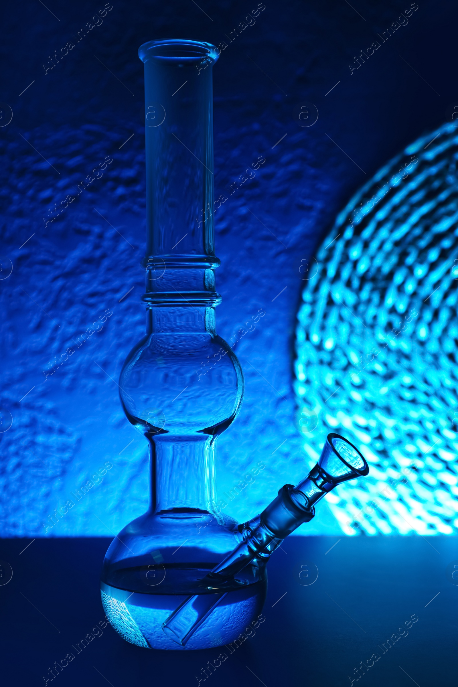 Photo of Glass bong on table, toned in blue. Smoking device