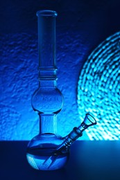 Glass bong on table, toned in blue. Smoking device