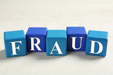 Photo of Word Fraud of cubes with letters on white wooden background