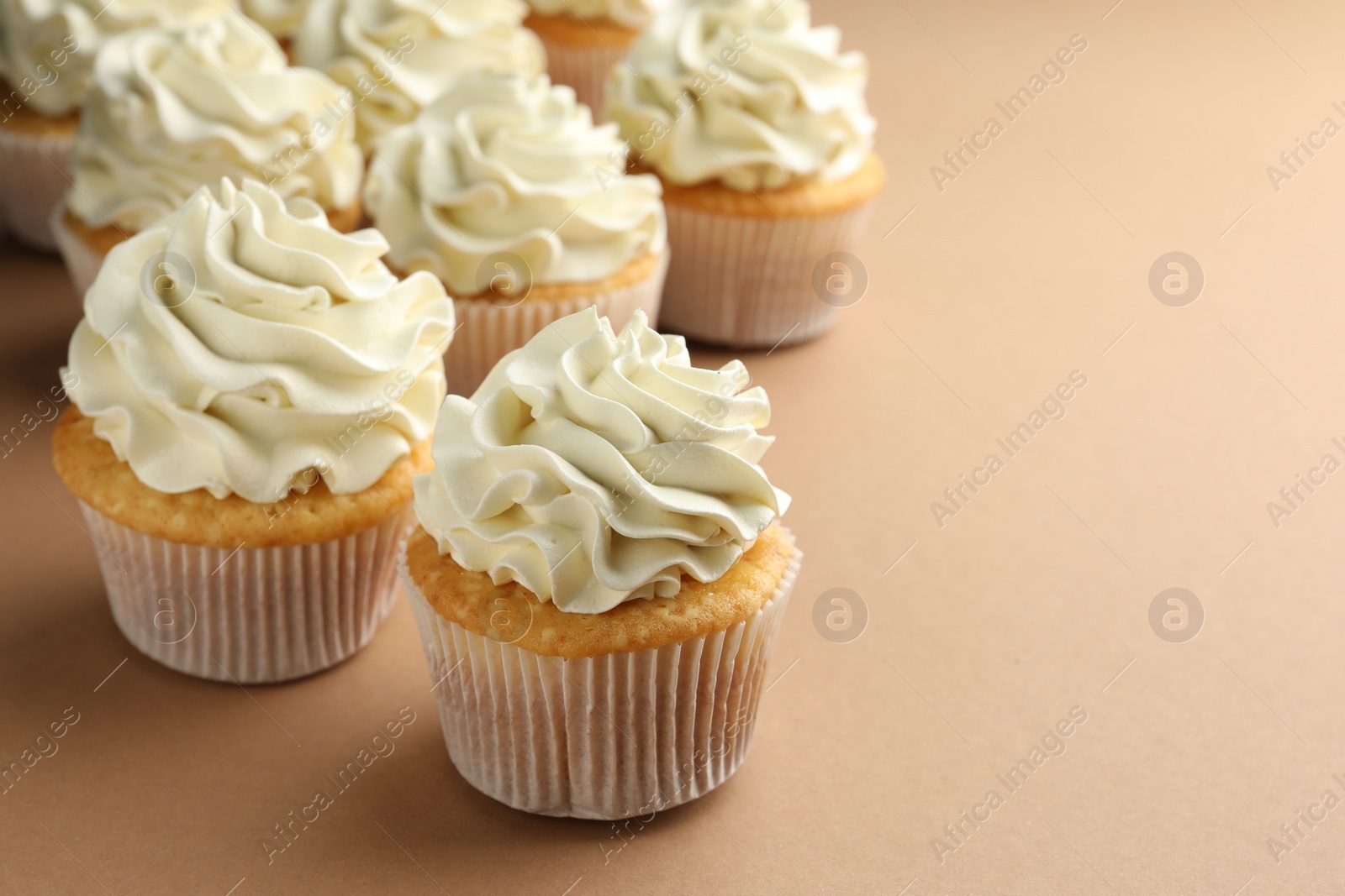 Photo of Tasty vanilla cupcakes with cream on beige table, closeup. Space for text