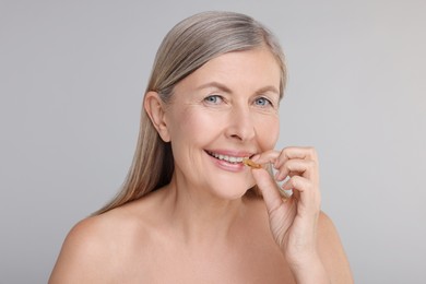 Beautiful woman taking vitamin capsule on grey background