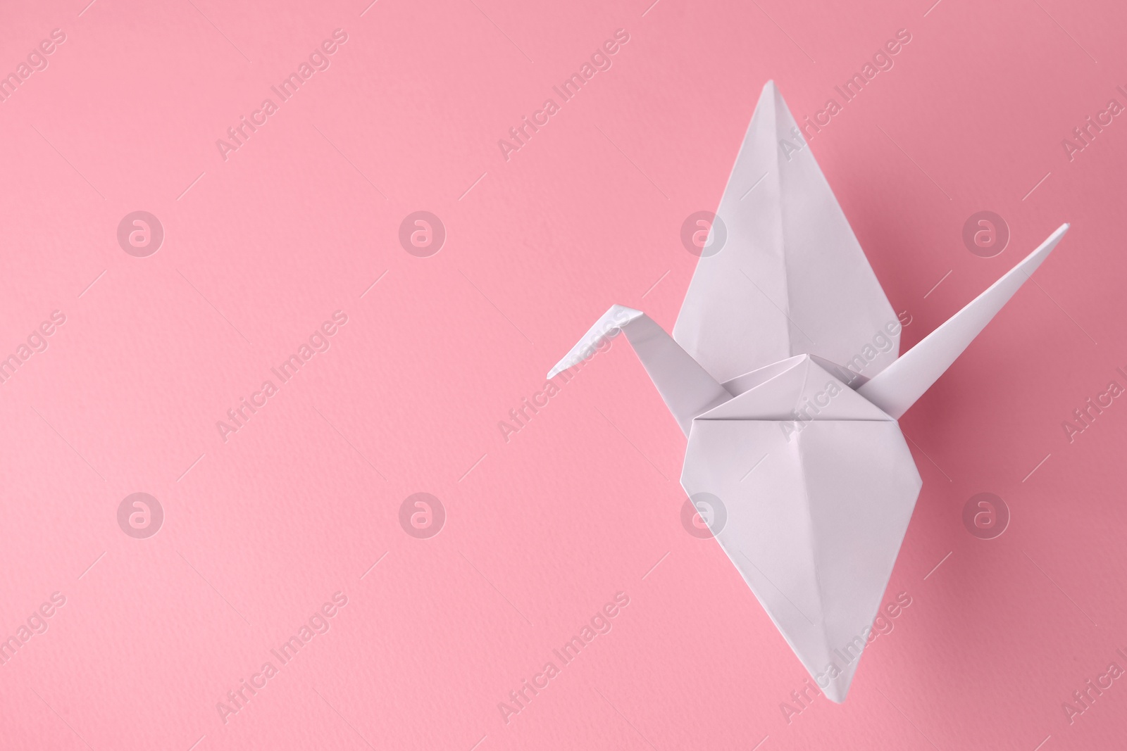 Photo of Origami art. Handmade paper crane on pink background, space for text