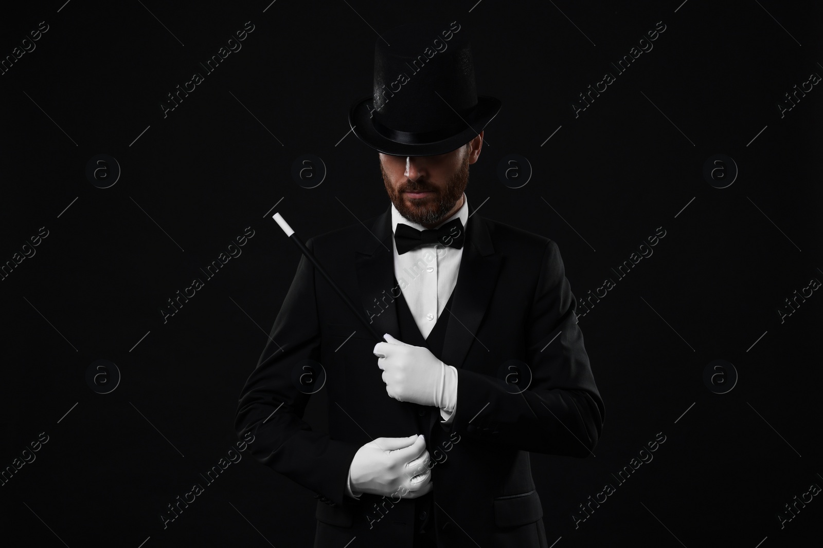 Photo of Magician in top hat holding wand on black background