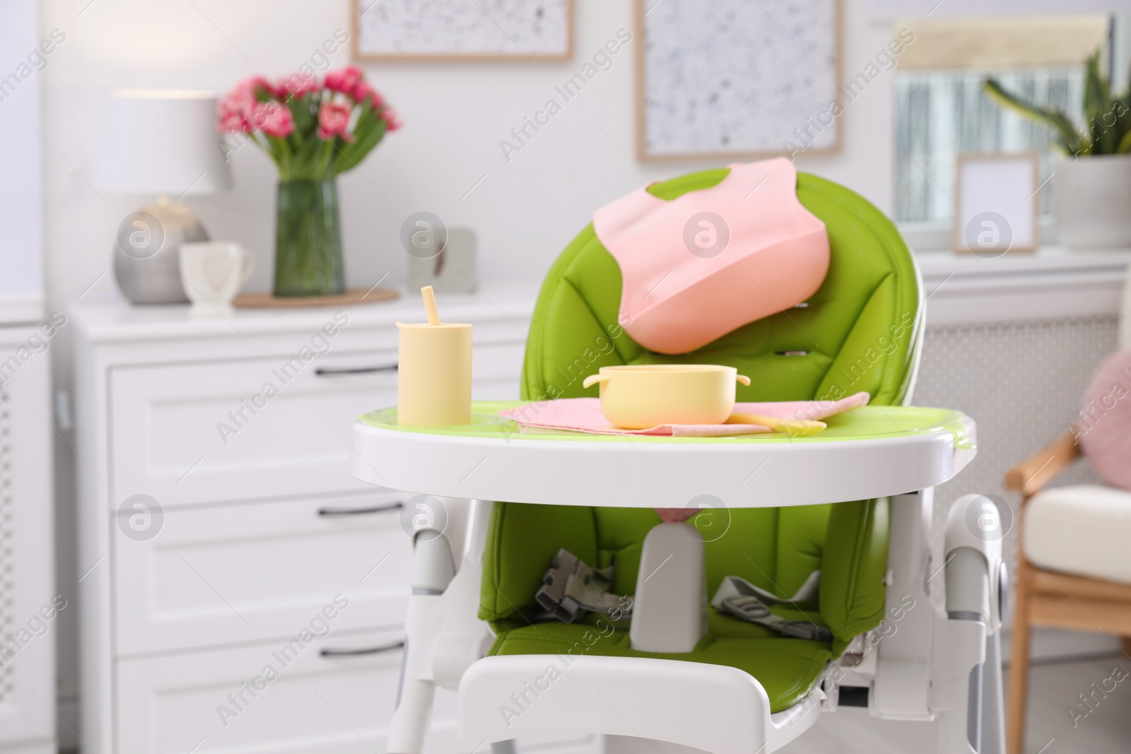 Photo of High chair with set of baby tableware on tray indoors