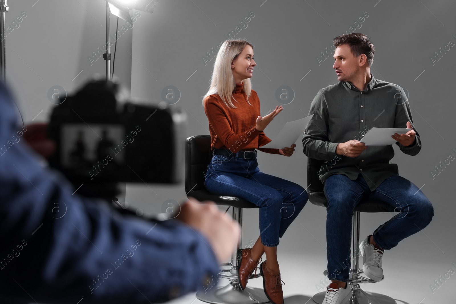 Photo of Casting call. Man and woman performing while camera operator filming them against grey background in studio