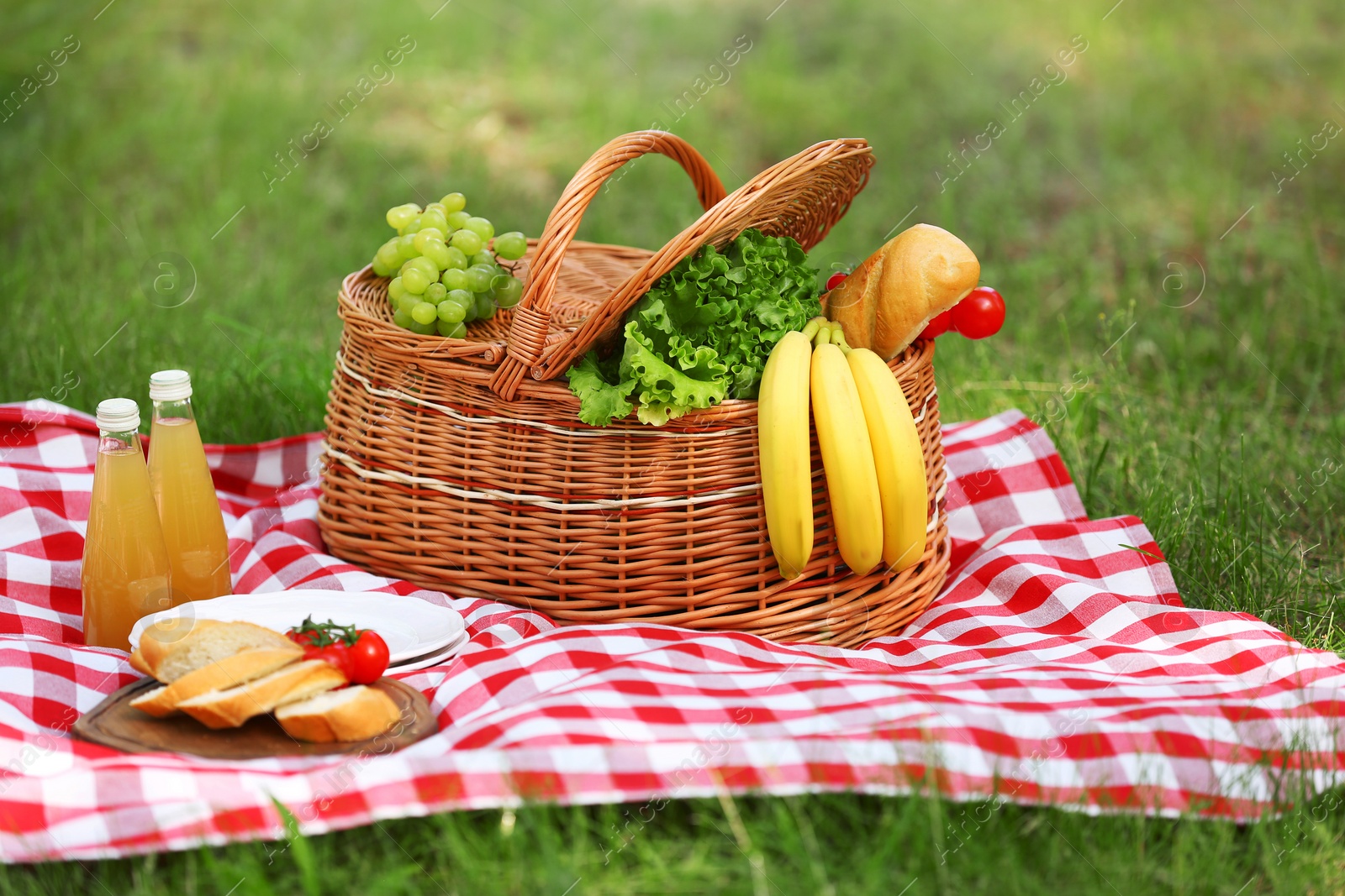 Photo of Wicker basket with food and juice on blanket in park. Summer picnic