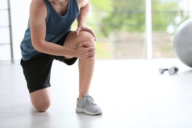 Man in sportswear suffering from knee pain at gym, closeup