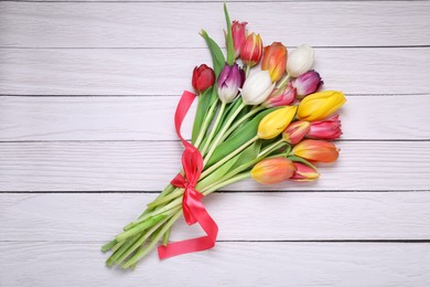 Photo of Bouquet of beautiful colorful tulip flowers tied with red ribbon on white wooden table, top view