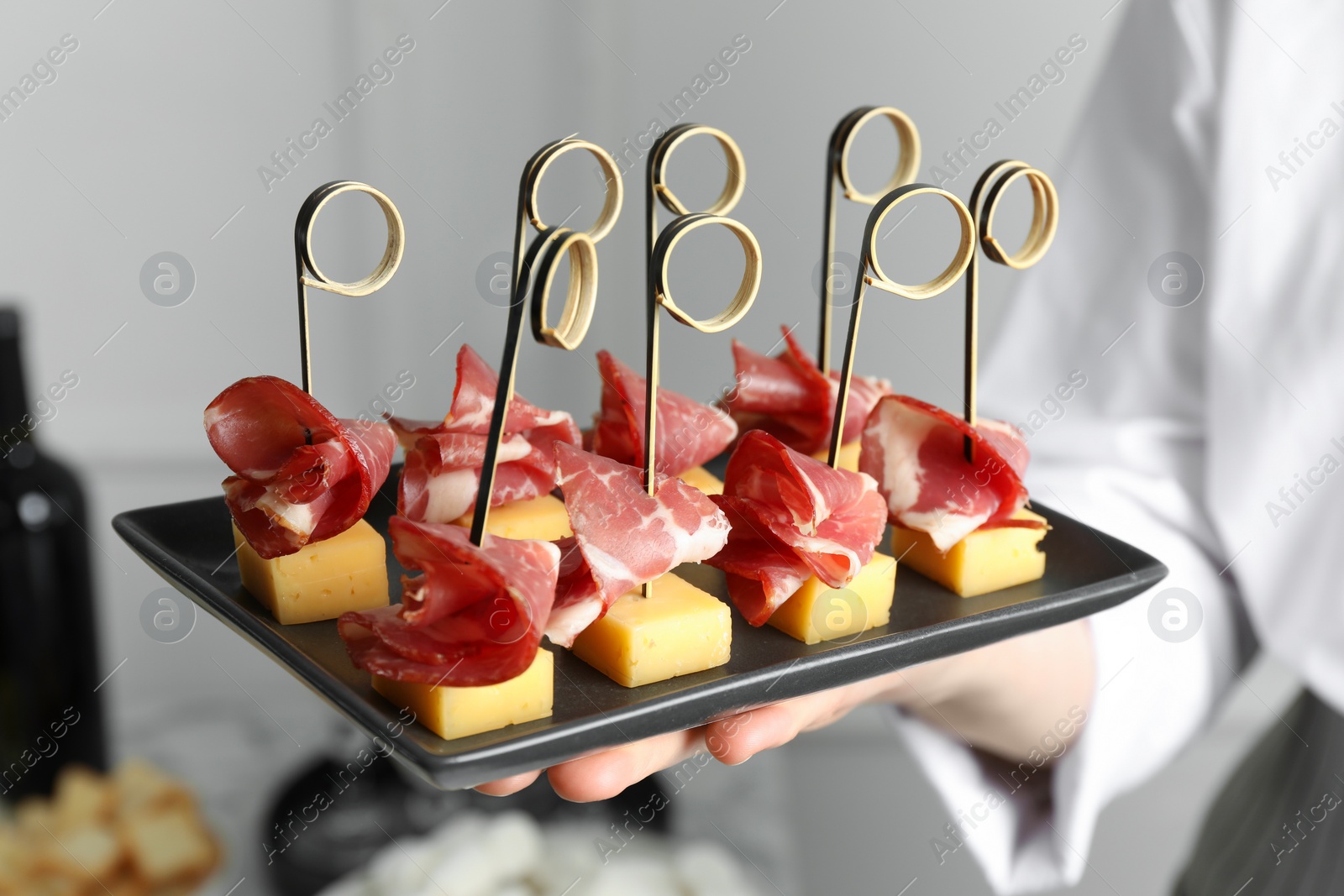 Photo of Woman holding plate of tasty canapes with ham and cheese indoors, closeup