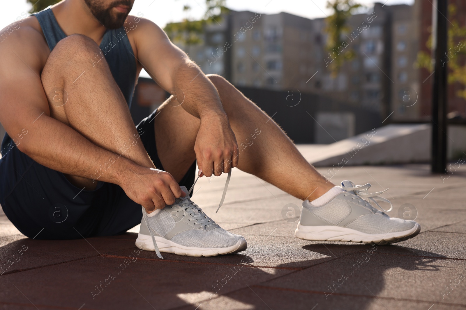 Photo of Man tying shoelaces before running outdoors on sunny day, closeup