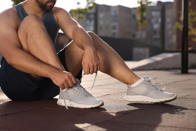 Man tying shoelaces before running outdoors on sunny day, closeup