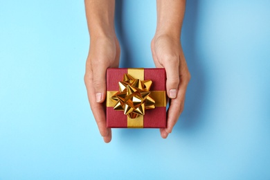 Woman holding beautiful gift box on blue background, top view