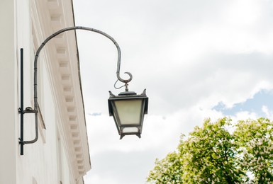 Photo of Vintage street lamp on wall of building against blue sky, low angle view. Space for text