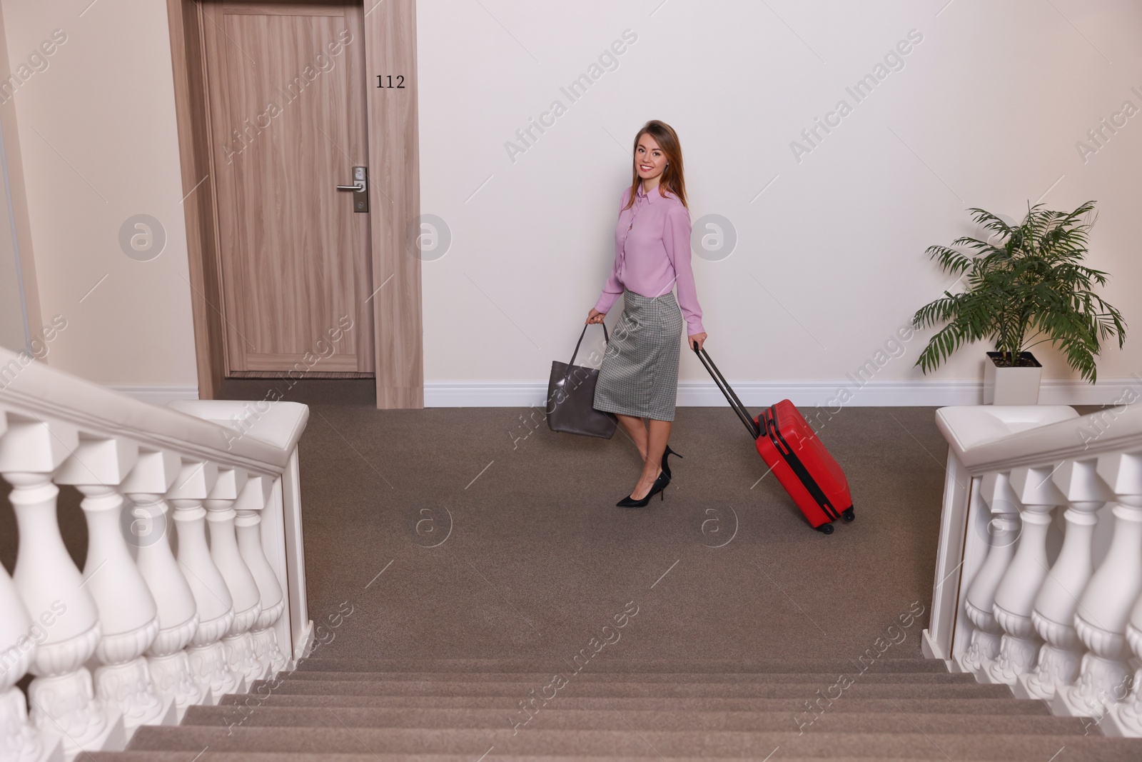 Photo of Businesswoman with red suitcase in hotel corridor, above view