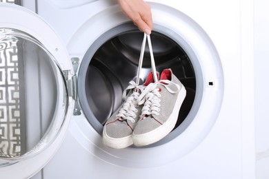 Photo of Woman putting pair of sport shoes into washing machine, closeup