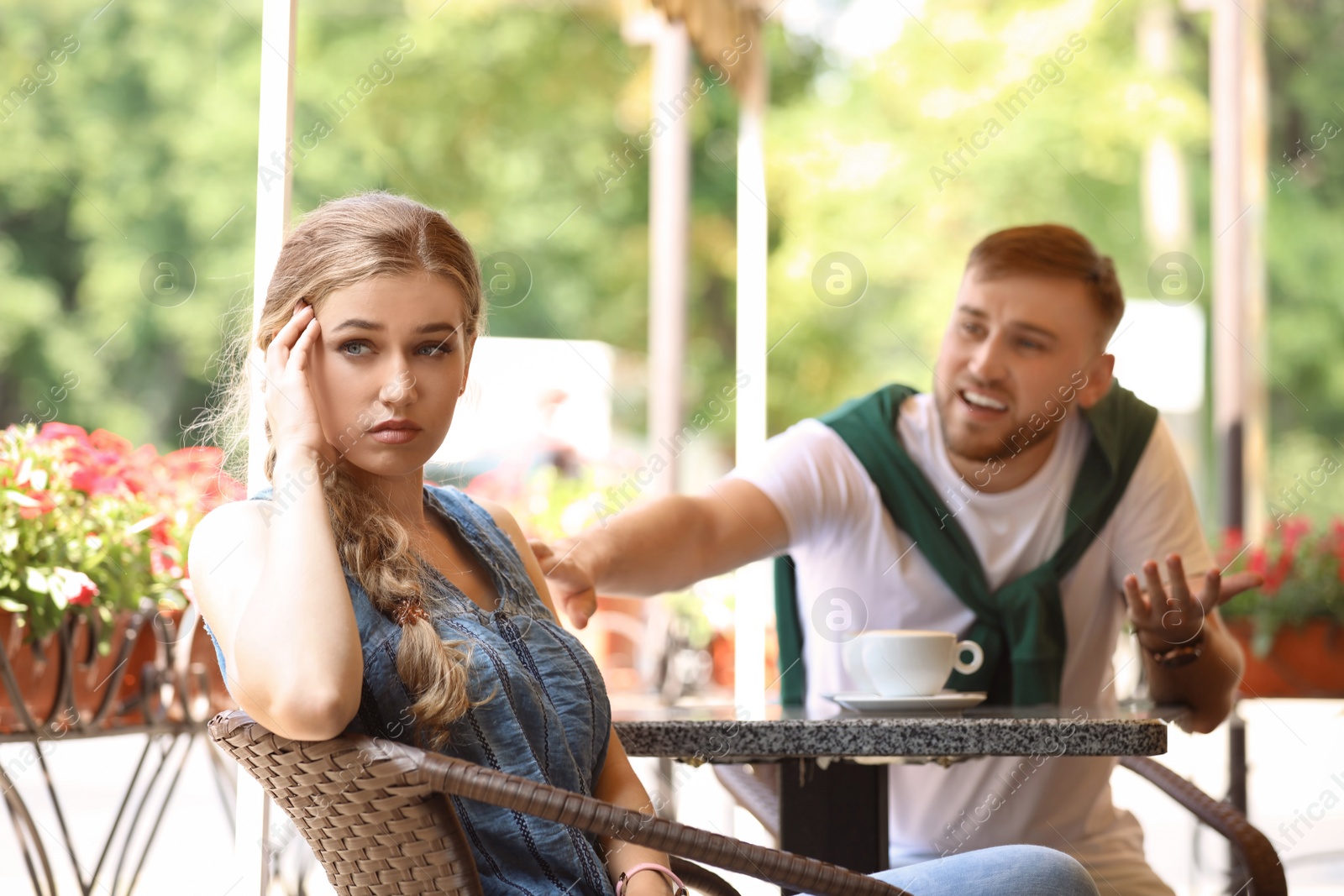 Photo of Young couple arguing while sitting in cafe, outdoors. Problems in relationship