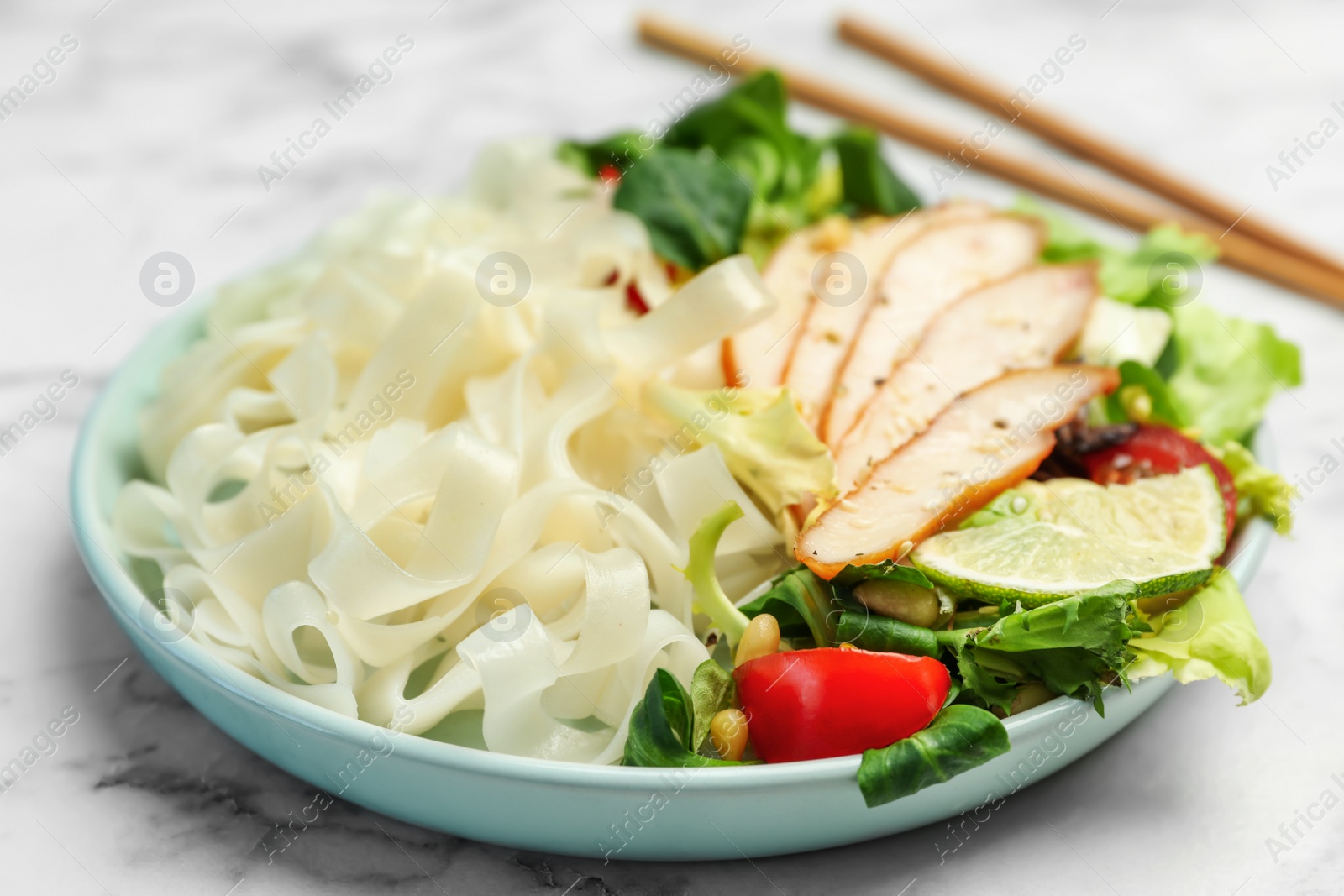 Photo of Tasty cooked rice noodles with chicken and vegetables on white marble table