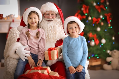Photo of Little children receiving gifts from authentic Santa Claus indoors