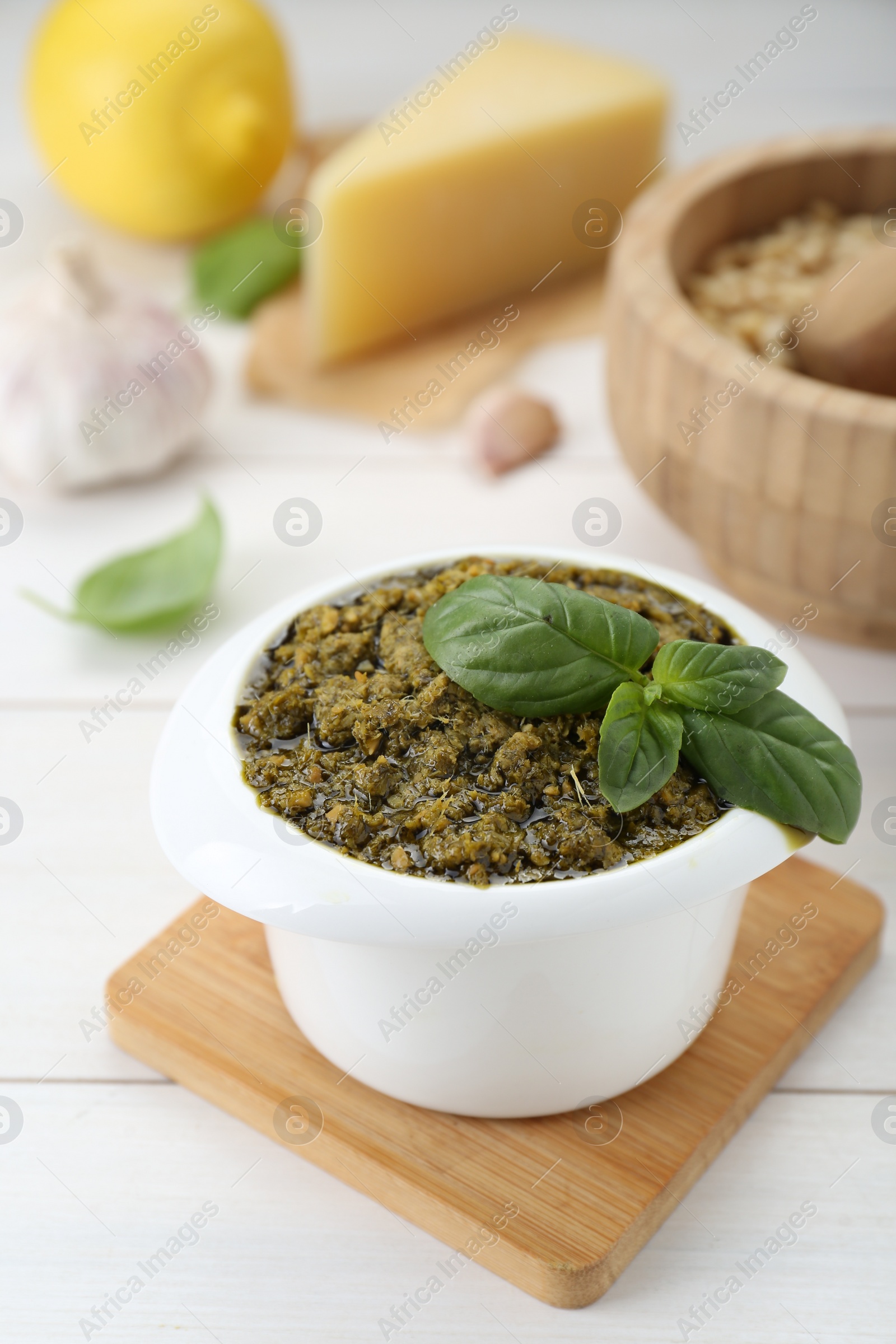 Photo of Delicious pesto sauce in bowl and ingredients on white wooden table