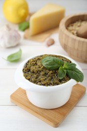 Delicious pesto sauce in bowl and ingredients on white wooden table