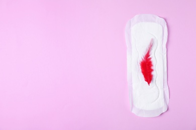 Menstrual pad and red feather on color background, top view with space for text. Gynecological care