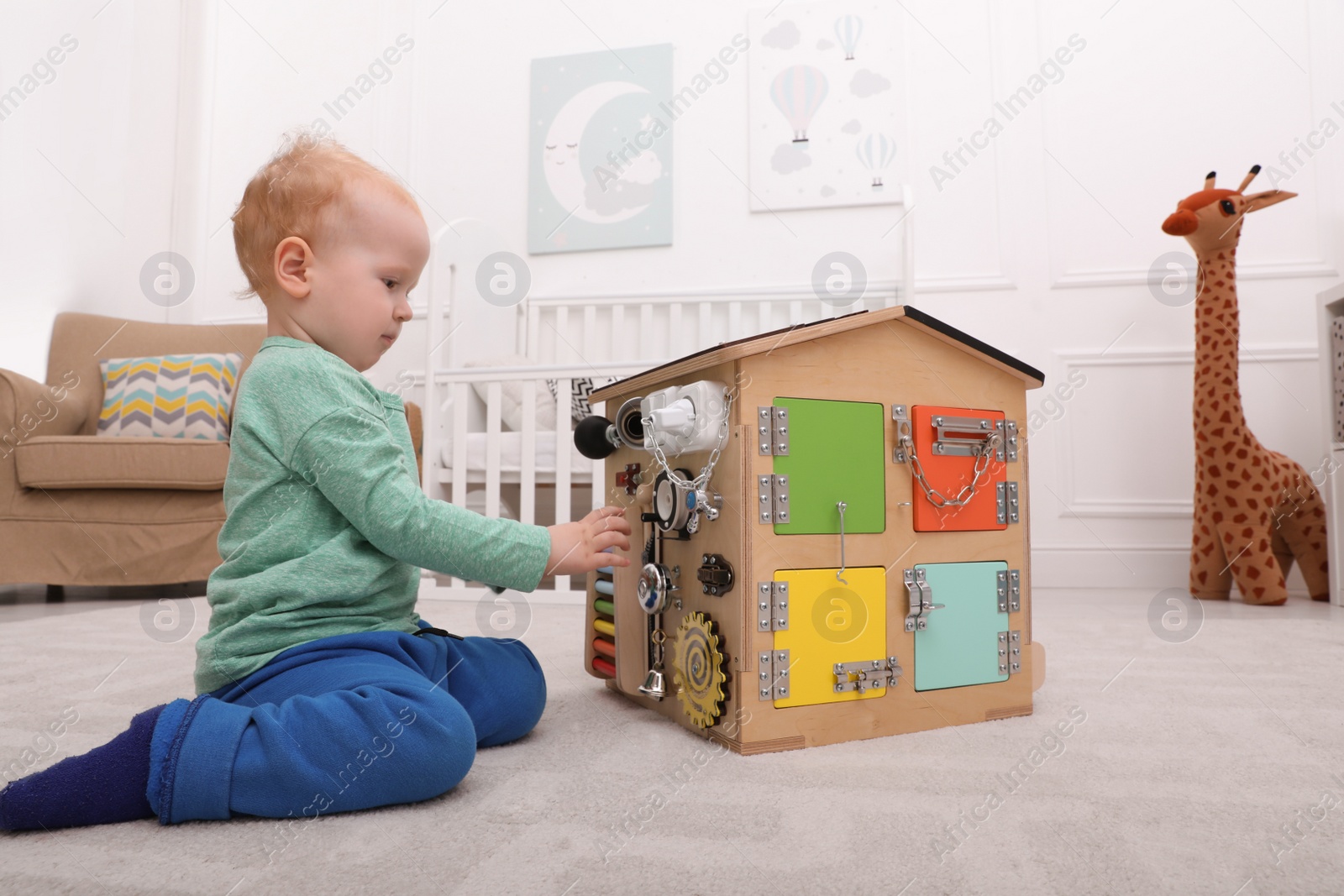 Photo of Cute little boy playing with busy board house on floor at home