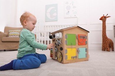 Photo of Cute little boy playing with busy board house on floor at home