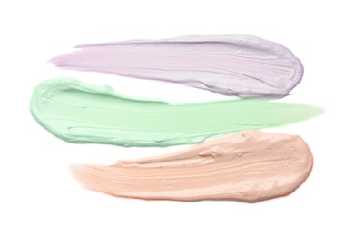 Photo of Strokes of pink, green and purple color correcting concealers isolated on white, top view
