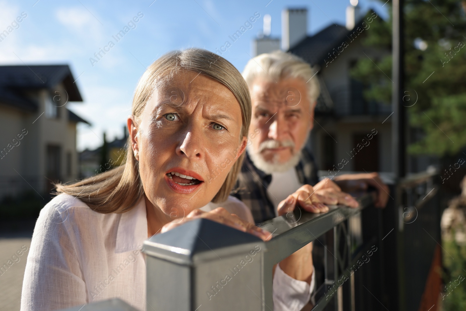 Photo of Concept of private life. Curious senior couple spying on neighbours over fence outdoors, selective focus