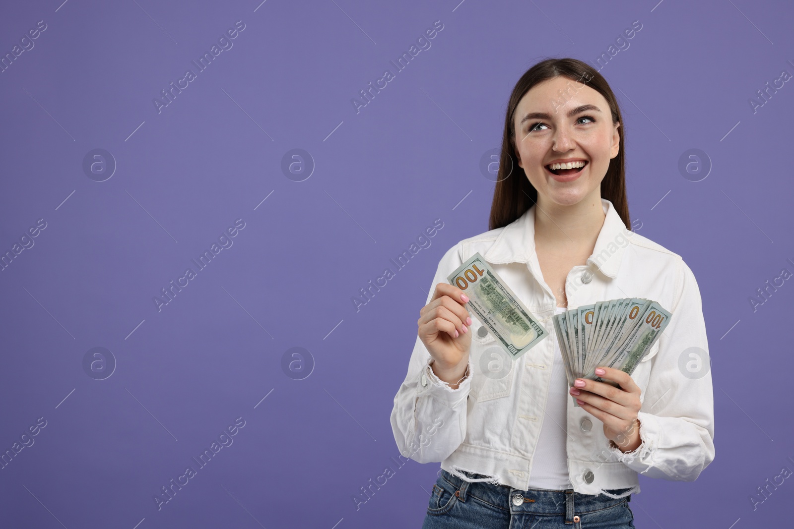 Photo of Happy woman with dollar banknotes on purple background, space for text