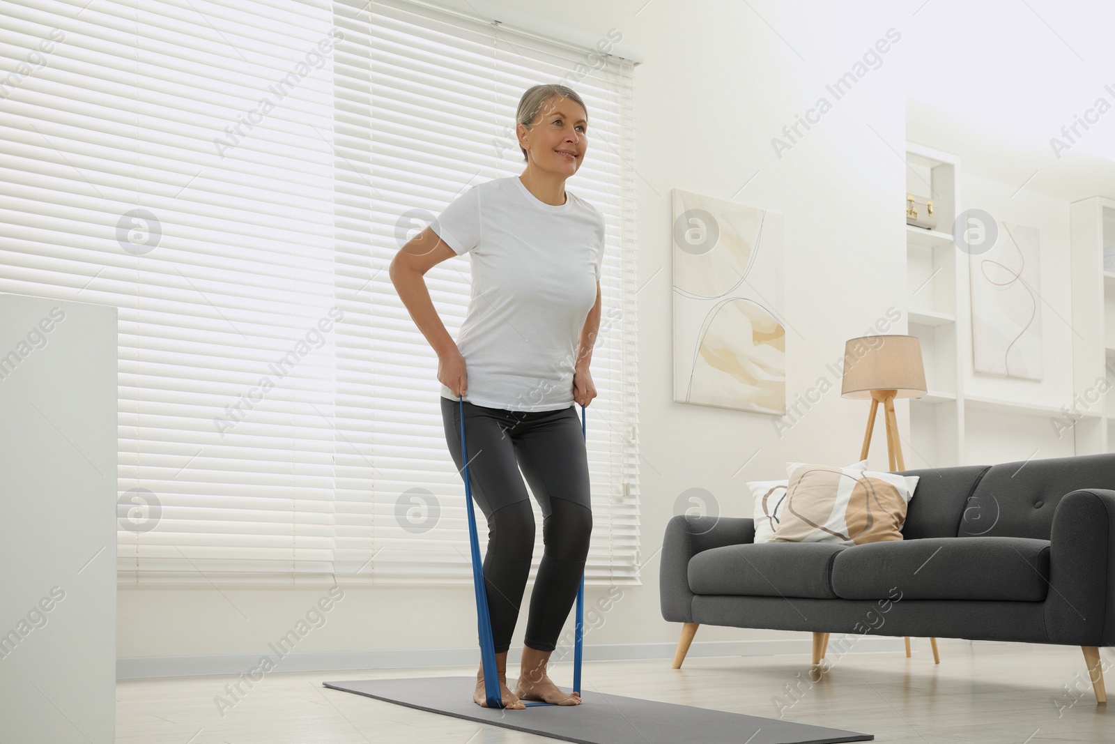 Photo of Senior woman doing exercise with fitness elastic band on mat at home