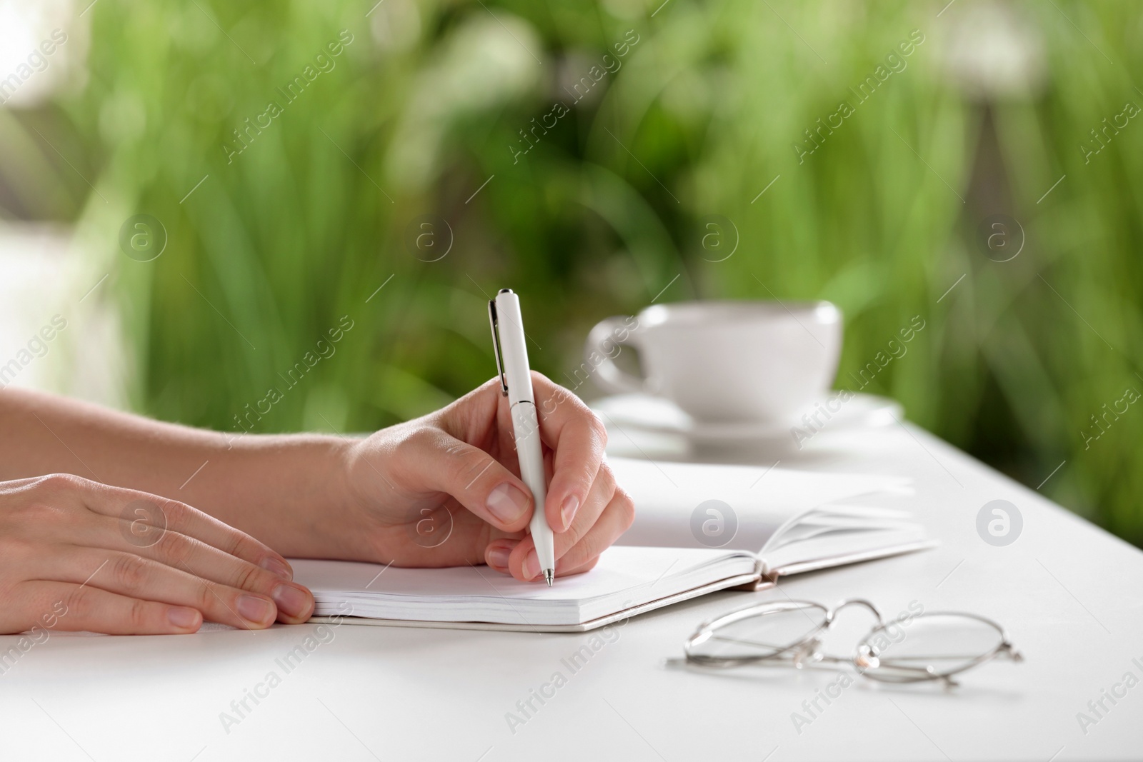 Photo of Woman writing in notebook at white table indoors, closeup