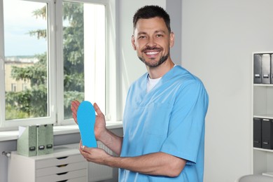 Photo of Handsome male orthopedist showing insole in hospital