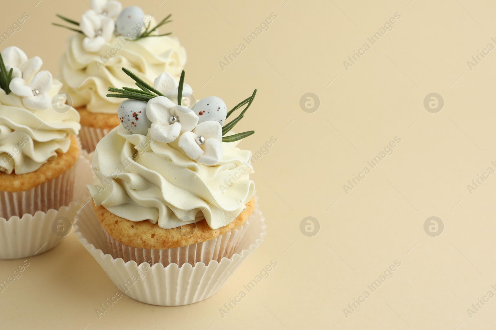 Photo of Tasty Easter cupcakes with vanilla cream on beige background, space for text