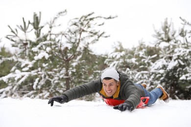 Photo of Happy man sledding outdoors on winter day. Christmas vacation