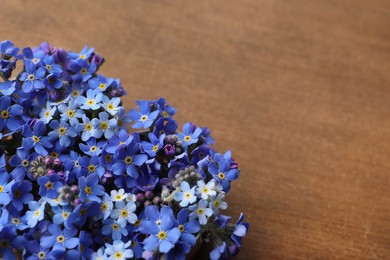 Photo of Beautiful blue forget-me-not flowers on wooden table. Space for text