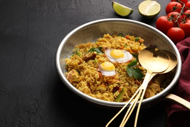 Photo of Tasty rice with meat, eggs and vegetables in frying pan near products on black textured table, space for text