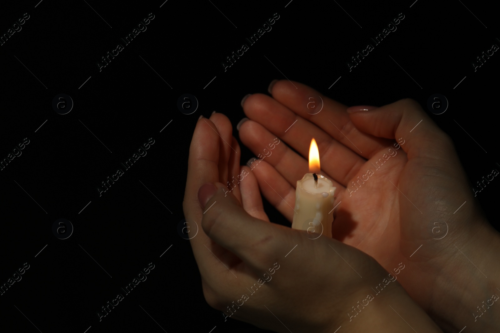 Photo of Woman holding burning candle in hands on black background, closeup. Space for text