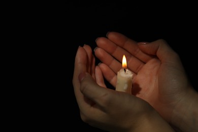 Woman holding burning candle in hands on black background, closeup. Space for text