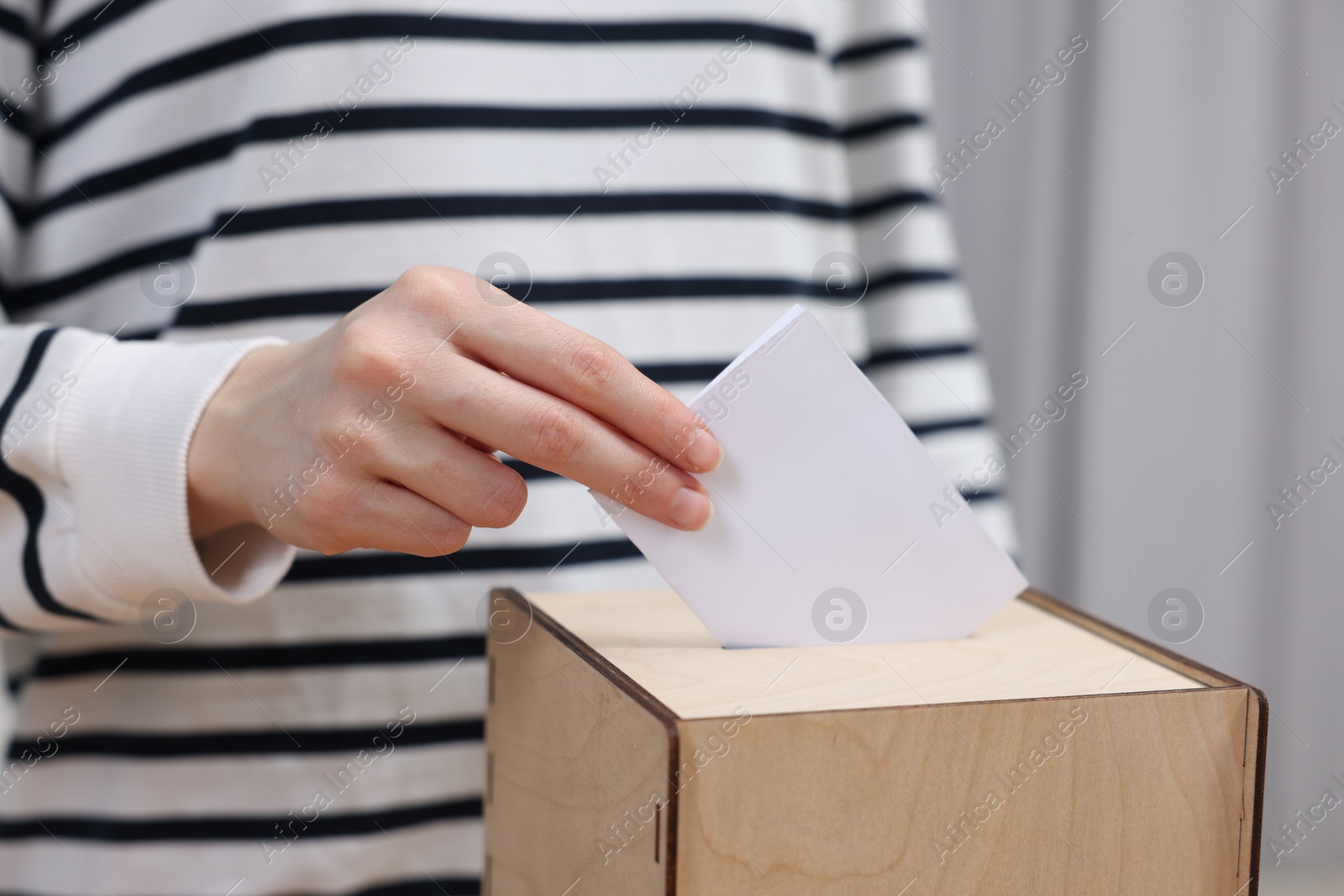 Photo of Woman putting her vote into ballot box on blurred background, closeup