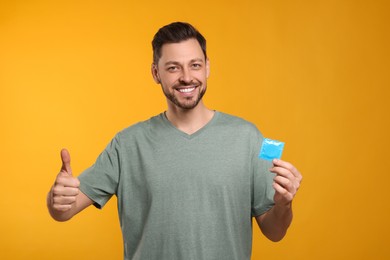 Happy man with condom showing thumb up on orange background