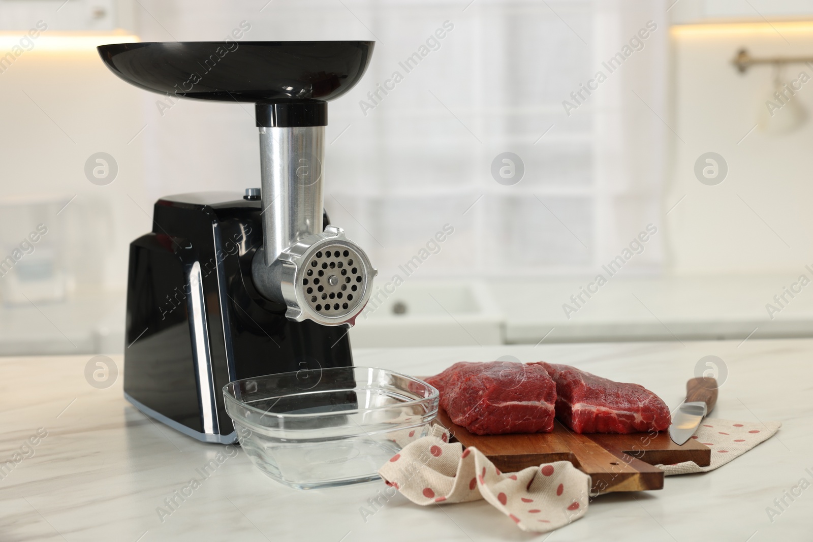 Photo of Electric meat grinder with beef on white marble table in kitchen