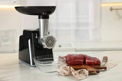 Electric meat grinder with beef on white marble table in kitchen