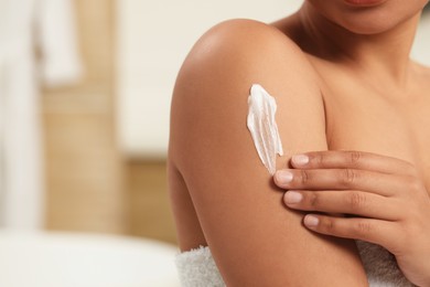 Photo of Young woman applying body cream onto arm in bathroom, closeup. Space for text